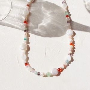 May include: A colourful beaded necklace with white, red, green, and blue beads. The necklace features large, white, oval-shaped beads.