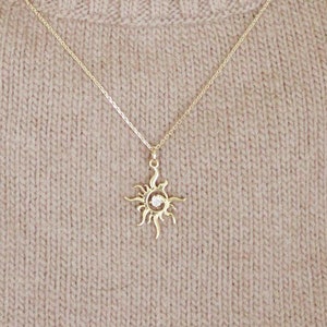 May include: A gold chain necklace with a sun pendant featuring a small clear stone in the centre.