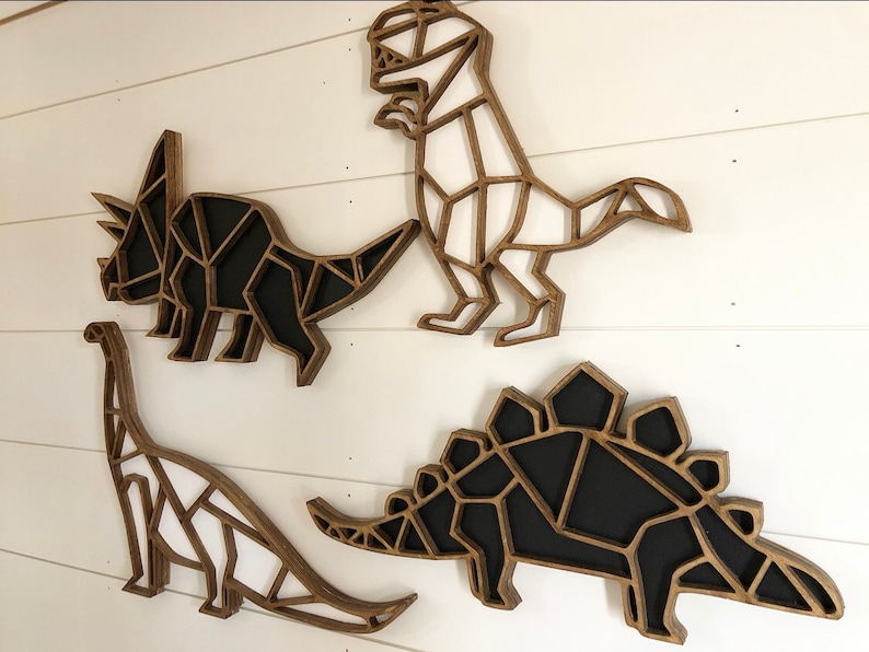 May include: Four wooden dinosaur wall decorations in a geometric style. The dinosaurs are a triceratops, a stegosaurus, a brachiosaurus, and a tyrannosaurus rex. The dinosaurs are painted in black and white.