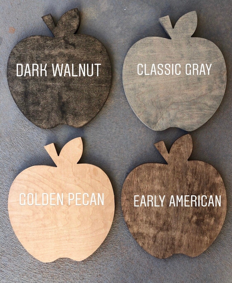 May include: Four wooden apple-shaped signs with different wood stains. The signs are labeled "Dark Walnut", "Classic Gray", "Golden Pecan", and "Early American".