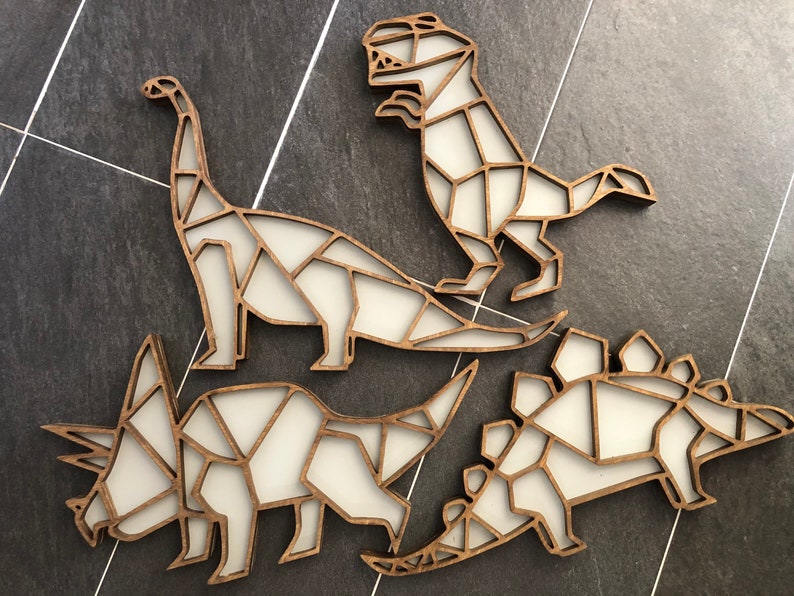 May include: Four wooden dinosaur wall decorations in a geometric style. The dinosaurs are a stegosaurus, a triceratops, a brachiosaurus, and a tyrannosaurus rex. The dinosaurs are all white with brown outlines.
