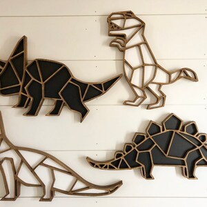 May include: Four wooden dinosaur wall decorations in a geometric style. The dinosaurs are painted black and white and are arranged in a row on a white wall.