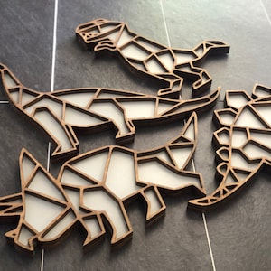 May include: Four wooden dinosaur wall decorations in a geometric style. The dinosaurs are a stegosaurus, a triceratops, a brachiosaurus, and a tyrannosaurus rex. The dinosaurs are all brown and white.