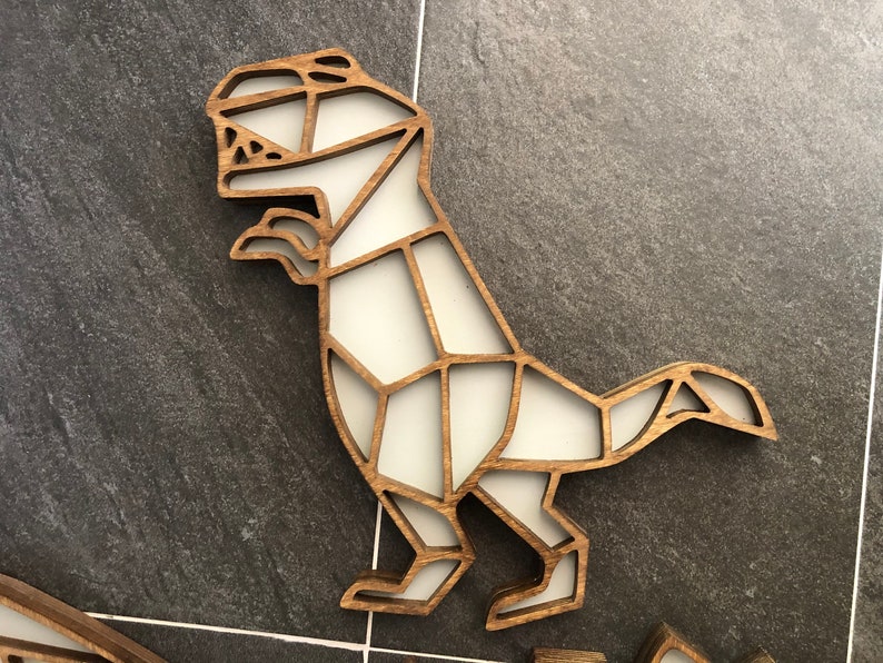 May include: A wooden dinosaur wall decor with a white geometric design. The dinosaur is standing on its hind legs with its tail curled up.