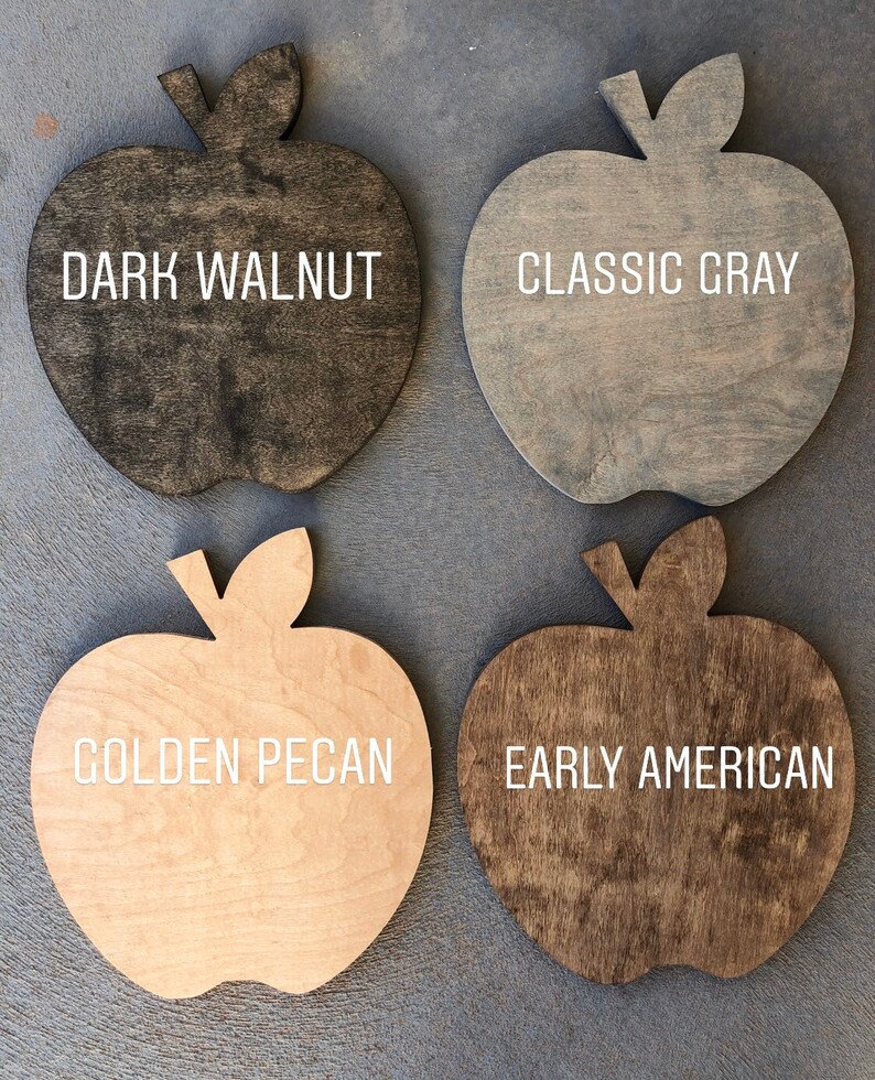 May include: Four wooden apple-shaped signs with different wood stains. The signs are labeled "Dark Walnut", "Classic Gray", "Golden Pecan", and "Early American".
