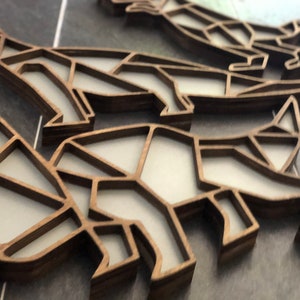May include: A close-up of a set of wooden dinosaur ornaments. The dinosaurs are made of a light brown wood and have a geometric design. The ornaments are stacked on top of each other.