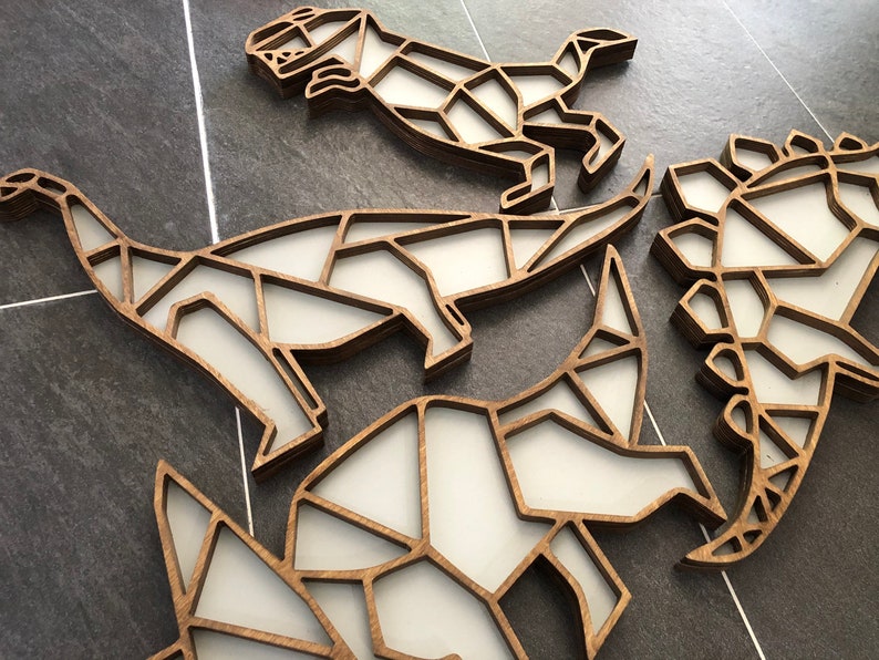 May include: Four wooden dinosaur wall decorations in a geometric style. The dinosaurs are made of layered wood and are painted white. They are arranged in a cluster on a gray tiled surface.