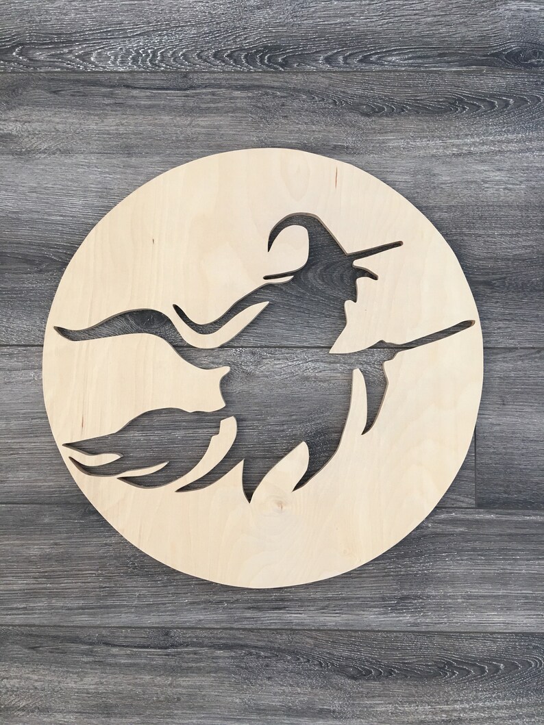 May include: A wooden cutout of a witch flying on a broomstick, set against a plain wooden background. The witch is silhouetted against a circular piece of wood.