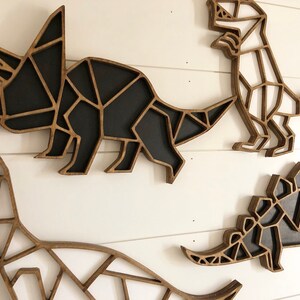 May include: Four wooden dinosaur wall decorations in a geometric style. The dinosaurs are a triceratops, a stegosaurus, a brachiosaurus, and a tyrannosaurus rex. The dinosaurs are all black and white.