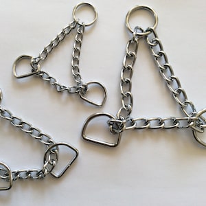May include: Three silver chain dog collars with D-rings. The collars are different sizes and are arranged in a triangular shape.