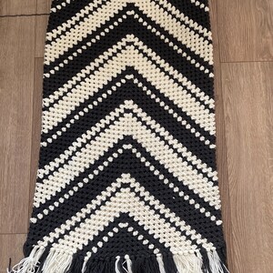 Puede incluir: Falda de crochet negra y crema con un patr&oacute;n de chevr&oacute;n. La falda tiene una cintura alta y una silueta larga y recta. El borde inferior est&aacute; rematado con una franja de hilo negro y crema.