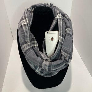 May include: A gray and white plaid infinity scarf with a cell phone tucked into the fabric.