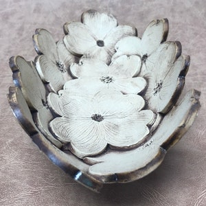 May include: A decorative bowl with a floral design. The bowl is shaped like a flower with multiple petals. The petals are white with dark brown edges and a dark brown center. The bowl is made of a ceramic material.