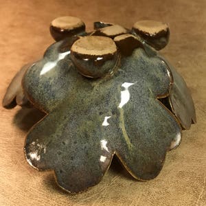 Puede incluir: Un cuenco artesanal de cer&aacute;mica con forma de hoja, con un esmalte brillante moteado azul-verdoso. El cuenco presenta detalles redondeados en relieve en un esmalte marr&oacute;n contrastante. Los bordes del cuenco est&aacute;n ligeramente levantados, creando una forma org&aacute;nica &uacute;nica.