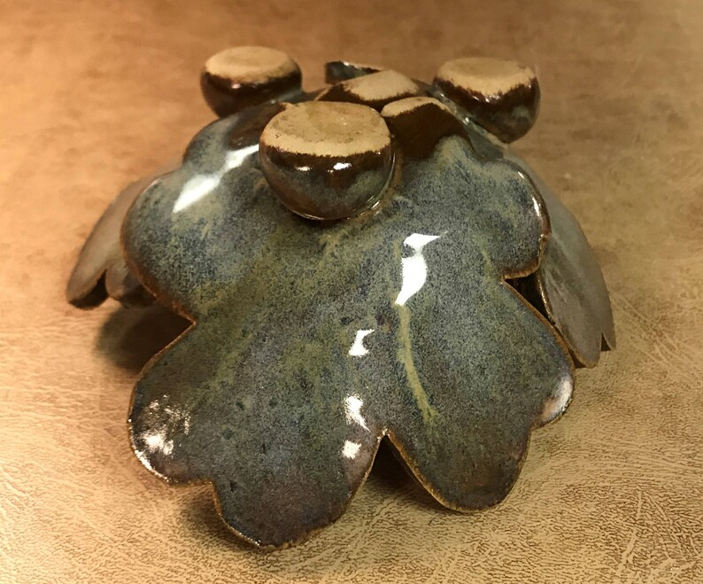 Puede incluir: Un cuenco artesanal de cer&aacute;mica con forma de hoja, con un esmalte brillante moteado azul-verdoso. El cuenco presenta detalles redondeados en relieve en un esmalte marr&oacute;n contrastante. Los bordes del cuenco est&aacute;n ligeramente levantados, creando una forma org&aacute;nica &uacute;nica.