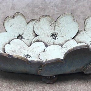 May include: A ceramic bowl with a floral design. The bowl is shaped like a flower with white petals and a dark gray base. The bowl is approximately 12 inches long and 8 inches wide.