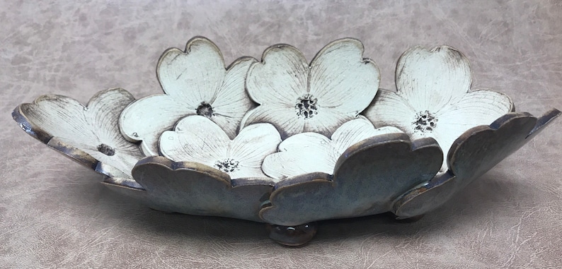 May include: A ceramic bowl with a floral design. The bowl is shaped like a flower with white petals and a dark gray base. The bowl is approximately 12 inches long and 8 inches wide.