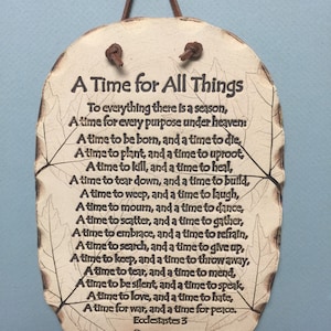 May include: Oval-shaped decorative plaque with the text "A Time for All Things" and a poem from Ecclesiastes 3. The plaque is off-white with a brown leather cord for hanging. Leaf-like designs frame the text.
