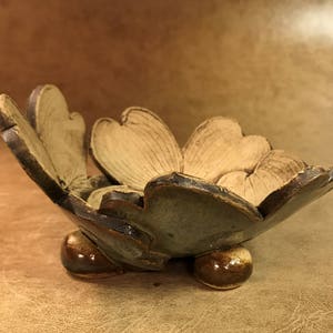 Puede incluir: Un cuenco de cer&aacute;mica hecho a mano con un dise&ntilde;o floral. El cuenco tiene un interior marr&oacute;n claro y un exterior marr&oacute;n oscuro y verde. Se apoya sobre tres peque&ntilde;os pies redondeados, mostrando una est&eacute;tica art&iacute;stica &uacute;nica.