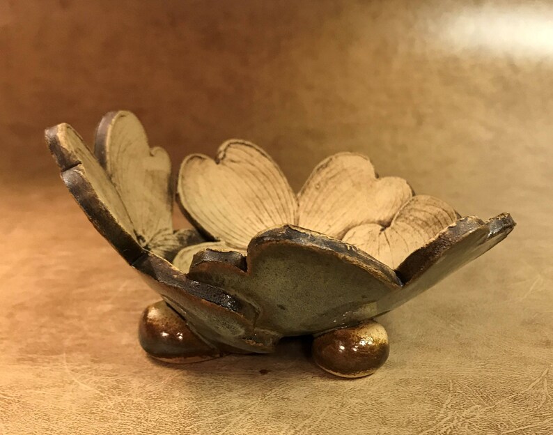 Puede incluir: Un cuenco de cer&aacute;mica hecho a mano con un dise&ntilde;o floral. El cuenco tiene un interior marr&oacute;n claro y un exterior marr&oacute;n oscuro y verde. Se apoya sobre tres peque&ntilde;os pies redondeados, mostrando una est&eacute;tica art&iacute;stica &uacute;nica.