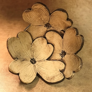 Puede incluir: Una escultura floral de cer&aacute;mica con tres flores estilizadas con p&eacute;talos en forma de coraz&oacute;n. Las flores son de color crema con contornos y centros marr&oacute;n oscuro. La escultura tiene un aspecto r&uacute;stico y hecho a mano.