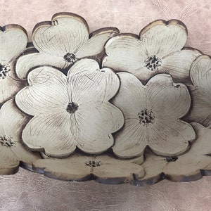May include: A decorative, floral-shaped serving dish. The dish is composed of multiple cream-colored, stylized flower shapes with brown edges and centers. The dish is set against a textured, light pink background.