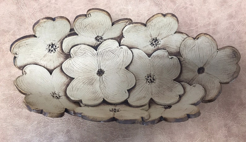 May include: A decorative, floral-shaped serving dish. The dish is composed of multiple cream-colored, stylized flower shapes with brown edges and centers. The dish is set against a textured, light pink background.
