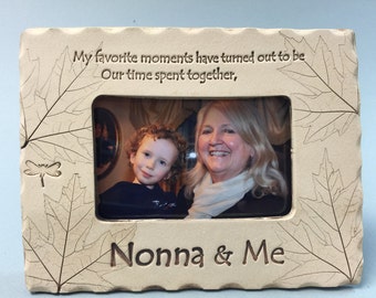 May include: Beige rectangular picture frame with a photo of a woman and a child. The frame has leaf and dragonfly designs. Text on the frame reads "My favorite moments have turned out to be Our time spent together, Nonna & Me."