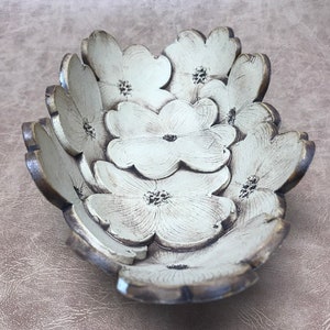 May include: A decorative bowl shaped like overlapping flowers. The bowl is painted in a cream color with brown edges, and each flower has a detailed center. The bowl is designed to hold small items and adds a touch of nature-inspired decor.