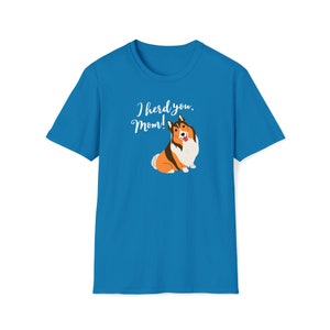 Op de afbeelding: Een helderblauwe t-shirt met een cartoon illustratie van een hond met bruin, wit en oranje haar. De tekst "I herd you, Mom!" staat in een sierlijk lettertype boven de hond.