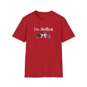 Op de afbeelding: Rood T-shirt met de tekst "I'm Sheltied" in witte letters en een cartoon afbeelding van twee Shetland Sheepdogs.