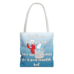 May include: A blue and white tote bag with a cartoon lobster wearing a chef's hat and holding a ladle. The text on the bag reads "Not all who roder are lost Some are just looking for a good crawfish boil."