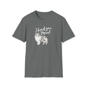 Op de afbeelding: Donkergrijs t-shirt met een aquarel illustratie van een Sheltie hond. De tekst "I herd you, Mom!" staat boven de hond. Het shirt heeft een ronde hals.