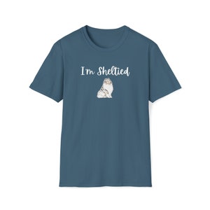 Op de afbeelding: Een donkerblauw t-shirt met de tekst "I'm Sheltied" in witte letters en een kleine illustratie van een sheltie-hond in het midden.