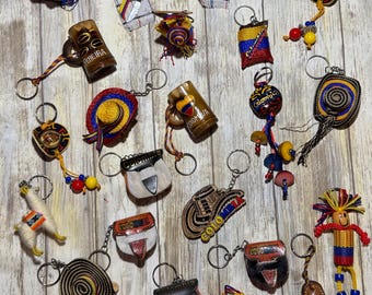 May include: A collection of 20 colorful Colombian keychains featuring various designs, including a llama, a traditional hat, a leather pouch, a beer mug, and a doll. The keychains are made of leather, fabric, and metal.
