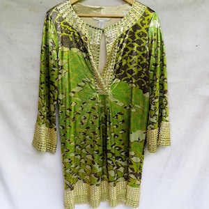 May include: A lime green and dark brown animal print tunic featuring three-quarter length sleeves, a deep V-neckline with a keyhole opening, and gold-toned metallic embellishments along the neckline, sleeve cuffs, and the bottom hemline.