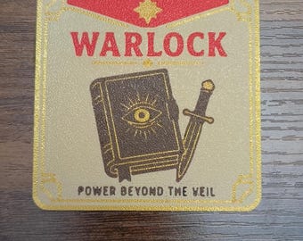 May include: A square coaster with a light tan background and a gold border. It features the red text WARLOCK above an illustration of a brown book with an eye symbol and a dagger. The text POWER BEYOND THE VEIL is printed in black at the bottom.