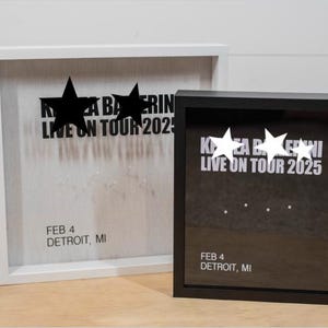 May include: Two white picture frames with black lettering. The top frame has a white background and the bottom frame has a black background. Both frames have the text "KYA BALLERINI LIVE ON TOUR 2025" and "FEB 4 DETROIT, MI".