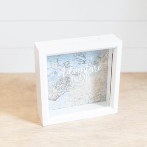 May include: White wooden box with a glass front, featuring a vintage world map and the text "Adventure Awaits".