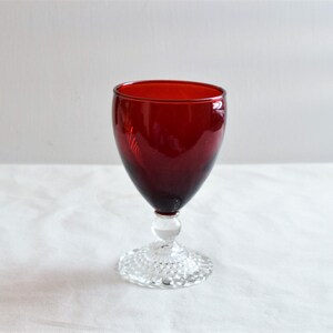 May include: A red glass goblet with a clear, textured base. The goblet is a traditional style with a round bowl and a stem.