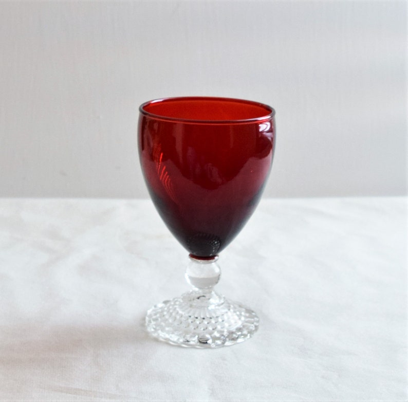 May include: A red glass goblet with a clear, textured base. The goblet is a traditional style with a round bowl and a stem.