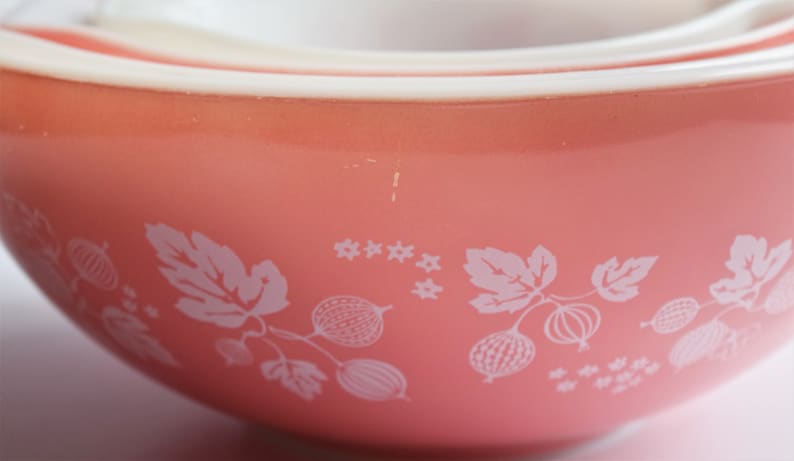 May include: A set of three pink mixing bowls with a white gooseberry pattern. The bowls are nested inside each other.