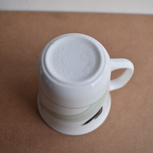 May include: White ceramic mug with a curved handle, featuring a design of green and black curved lines. The bottom of the mug has the text "CO. RIWING USA 29 WAVE OK".