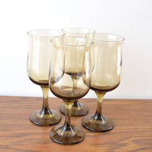 Puede incluir: Cuatro copas de vino ámbar vintage. Cada copa tiene un cuenco redondeado, un tallo delgado y una base circular. Las copas están dispuestas sobre una superficie de madera, mostrando su elegante diseño y estética vintage.