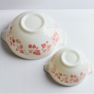 May include: Two white ceramic bowls with pink gooseberry designs. The bowls have handles on either side.
