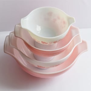 May include: A set of three pink and white mixing bowls with a floral design. The bowls are nested inside each other.