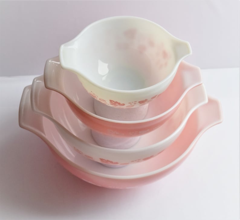 May include: A set of three pink and white mixing bowls with a floral design. The bowls are nested inside each other.
