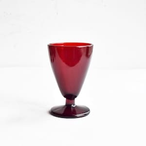 Puede incluir: Una copa de vidrio rojo oscuro con una base ancha y una parte superior estrecha. La copa está hecha de vidrio transparente con un tinte rojo.