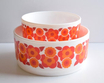May include: Two white nesting bowls with a red and orange floral pattern. The bowls are made of plastic and have a smooth, glossy finish.