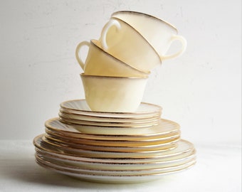 May include: A stack of white and gold rimmed vintage teacups and saucers. The cups are stacked on top of each other, with the top cup tilted slightly to the side. The saucers are stacked underneath the cups, with the top saucer slightly offset from the others.